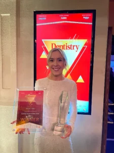 dental nurse winning two awards, and holding the awards in both hands, smiling 